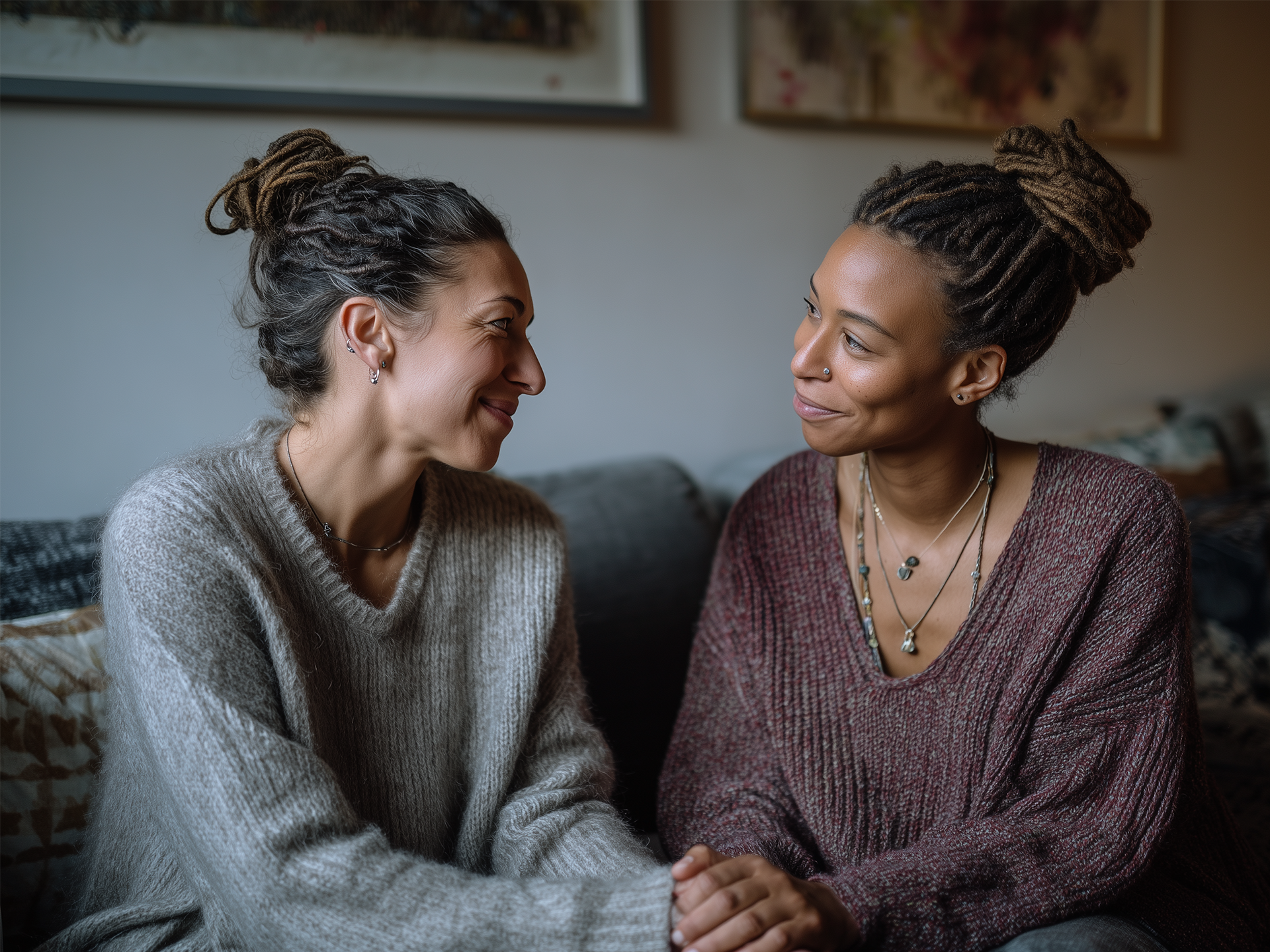 Two women sitting on sofa looking at eachother holding hands